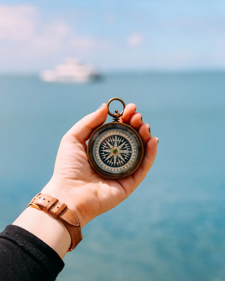Eine Hand hält einen Kompass vor dem Meer